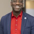 Dr. Julius Sokenu smiling, wearing a red shirt and blue spor