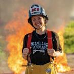 A young woman wearing a firefighter’s helmet and yellow pant