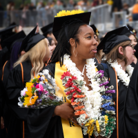 A smiling graduate holds a bouquet and wears colorful leis at the 2024 Ventura College Commencement Ceremony.