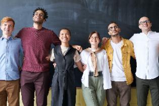 Four men and two women smiling in front of a chalkboard