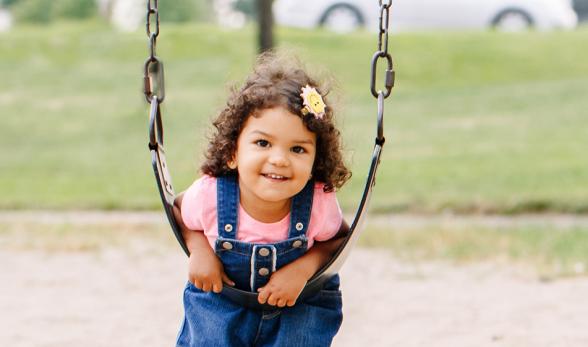 Little girl leaning on a swing at an outdoor park. 