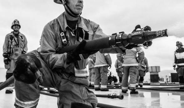 Jack Twitchell in full firefighter garb with a fire hose. 