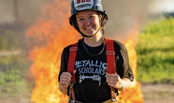 A young woman wearing a firefighter’s helmet and yellow pant