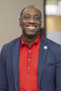 Dr. Julius Sokenu smiling, wearing a red shirt and blue spor