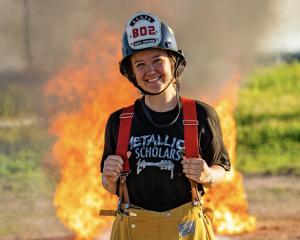 A young woman wearing a firefighter’s helmet and yellow pant